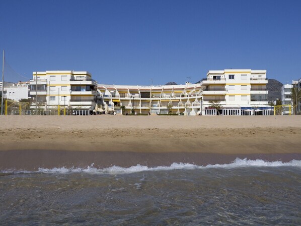 A beachfront hotel with multiple balconies, a sandy beach in the foreground, and clear skies. - Nice apartment in front of the sea in Roses Inmosantos Oasis E3 (Rosas / Roses)