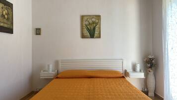 Una camera da letto con un letto, un comodino, un quadro appeso al muro e un vaso con fiori.