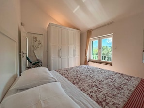 Un dormitorio con cama, armario, silla y ventana con vistas a zonas verdes.
