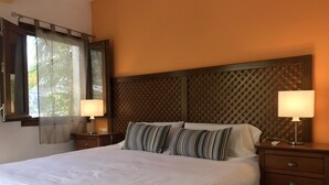Un lit bien fait, agrémenté d’oreillers à rayures, de deux lampes de chevet et d’une tête de lit en bois ornée d’un motif losangique.