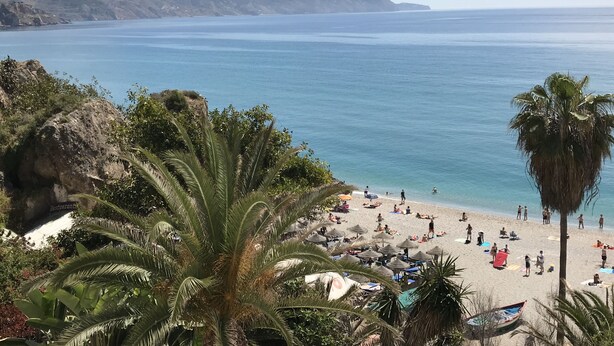 Une plage où des gens se prélassent au soleil, avec des parasols et un restaurant en arrière-plan.