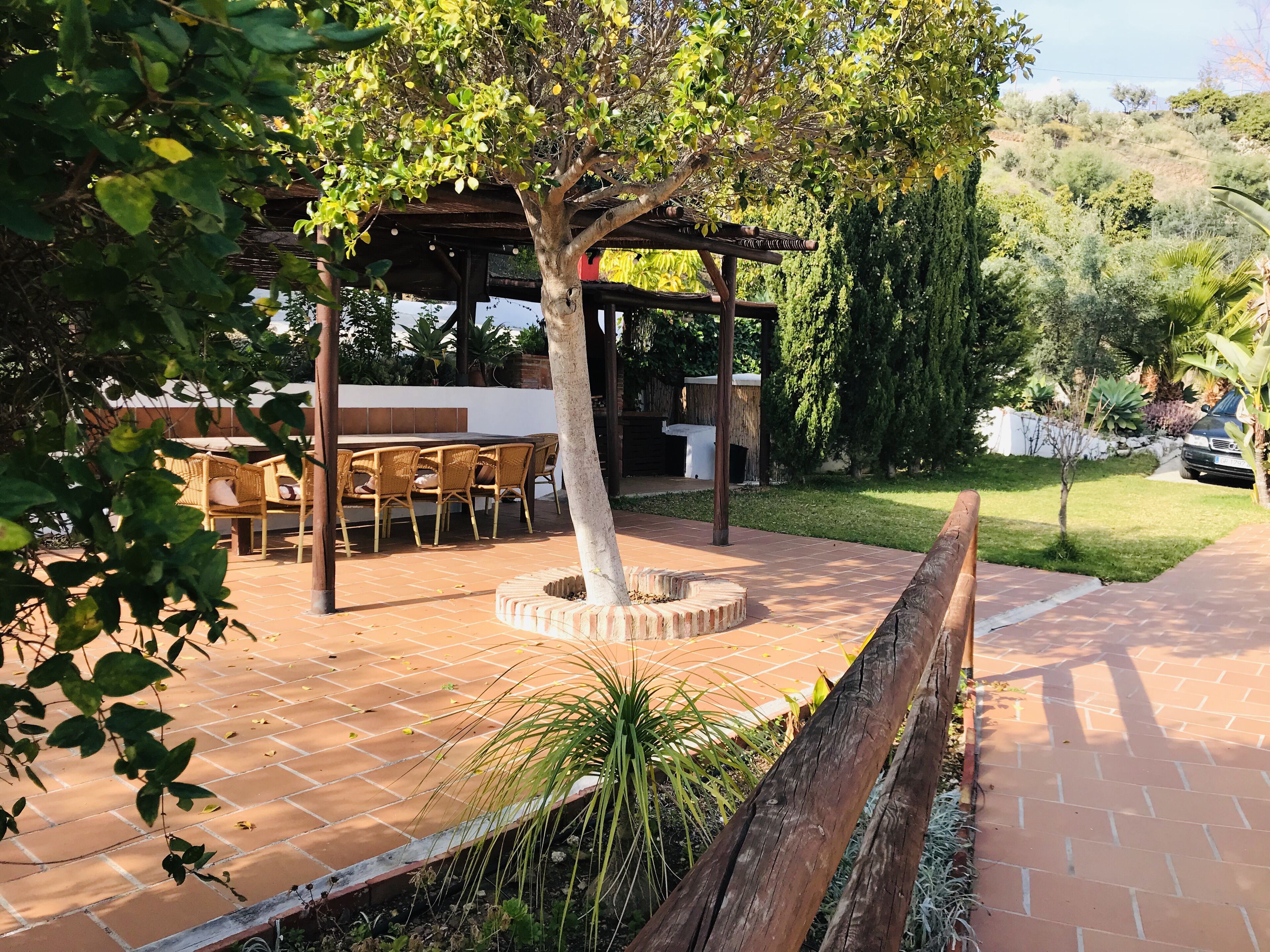 An outdoor patio area with a wooden pergola, a brick fire pit, and a dining table with chairs.