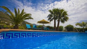 Une piscine bordée de mosaïques bleues, entourée de palmiers et de chaises longues.