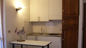 A kitchen with white cabinets, a gas stove, a sink, and a small table with a vase of flowers. - Apartment/ flat - Marina di grosseto (Marina di Grosseto)