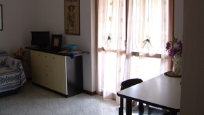 A living room with a sofa, a TV, a desk, and a dining table. - Apartment/ flat - Marina di grosseto (Marina di Grosseto)