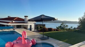 Una piscina con un flotador de flamenco rosa, un área de patio techada y vista al agua.