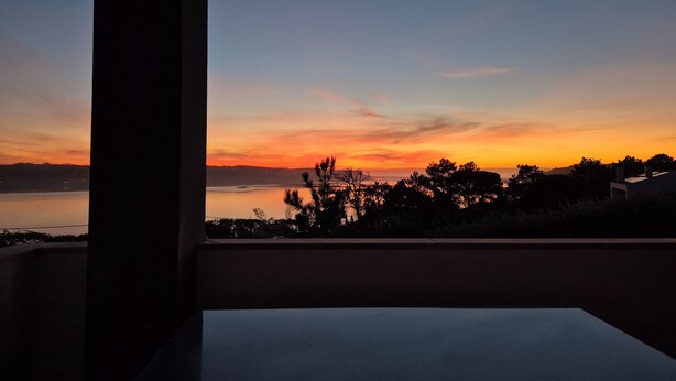 Vista del atardecer desde un balcón, con cielo despejado y siluetas de árboles.
