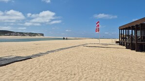 Una playa arenosa con una estructura de madera, una bandera y cielo despejado.