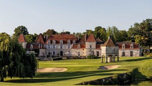 Un grand bâtiment historique doté de nombreuses tours et d’une pelouse bien entretenue, agrémentée d’un étang et de plusieurs bunkers de sable.