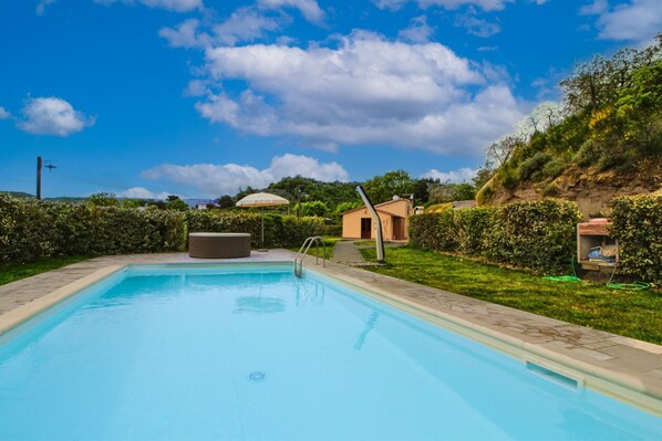 A swimming pool with a hot tub, surrounded by a grassy area and a small building.