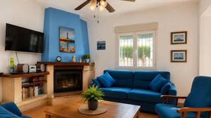 A living room with a blue sofa, a wooden coffee table, a fireplace, and a television. - Chipiona Corner semi-detached house on the beachfront (Chipiona)