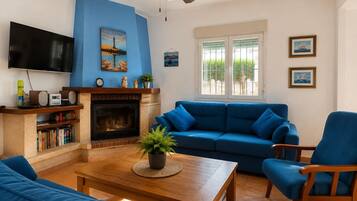 Een woonkamer met een blauwe bank, een houten salontafel, een open haard en een televisie.