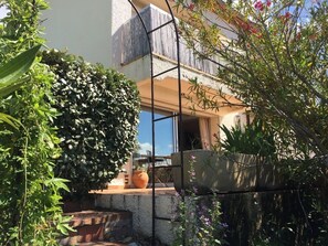 En gårdsplads med et træpergola, plantekrukker og udsigt til en bygning med balkon.