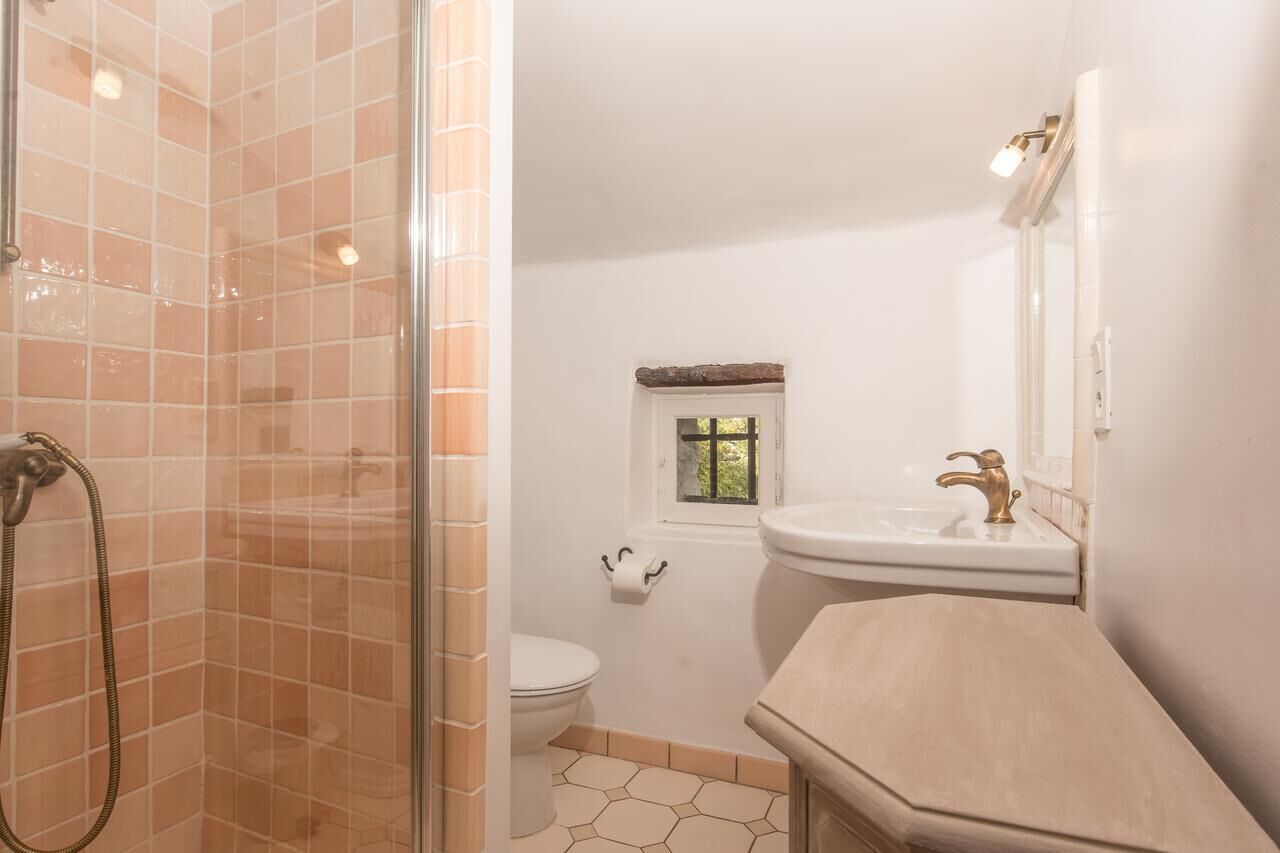 A bathroom with a glass shower enclosure, a toilet, a window, and a sink with a mirror.