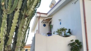 Ein Gebäude mit weißer Fassade, einem Balkon mit Topfpflanzen und einer Treppe, die zu einer oberen Ebene führt.