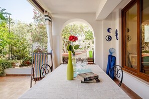 Un espace extérieur abrité, avec une table, des chaises, un livre et un vase de fleurs.