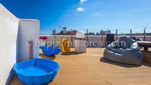 Una terraza en la azotea con una piscina de plástico azul, un tobogán amarillo y un sillón de pie de saco gris.