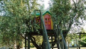 Una casa en un árbol con puerta roja y techo amarillo, construida sobre una plataforma de madera.