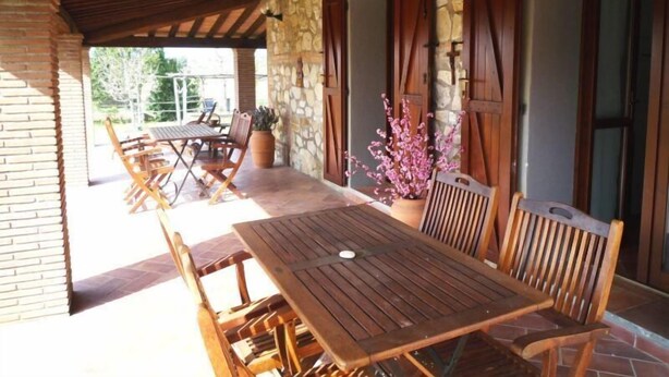 Un patio al aire libre con una mesa y sillas de madera, muros de piedra y una estructura de ladrillo.