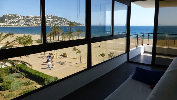 Une chambre dotée de grandes fenêtres donnant sur une plage, d’un balcon avec une balustrade et d’un lit avec un oreiller.