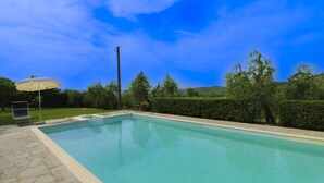 A rectangular swimming pool with a tiled edge, surrounded by a paved patio. There is a single lounge chair and an umbrella on the patio. - Ancient with private garden and swimming pool, characteristic and rustic style. Situated in the gree (Arezzo)