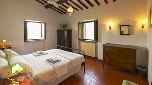A bedroom with a bed, dresser, two windows, and a radiator. - Ancient with private garden and swimming pool, characteristic and rustic style. Situated in the gree (Arezzo)