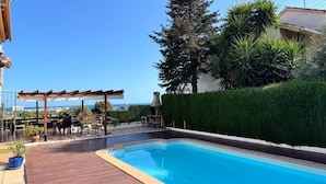 Een zwembad met houten terras, een pergola en uitzicht op zee.
