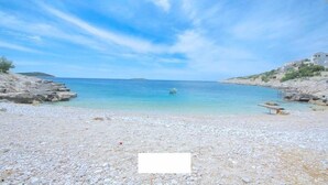 Une plage de galets bordée d’une eau d’un bleu limpide et d’un paysage rocheux.