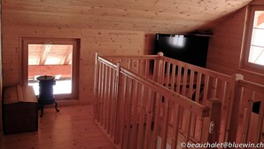 A wooden interior with a balcony, a black television, and a window. - La Tzoumaz, 'BeauChalet'. Large 8-person chalet, Ski In, ski out (La Tzoumaz)