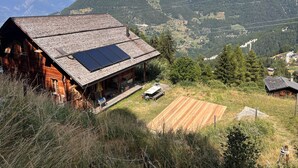 A rustic wooden cabin with a sloped roof and solar panels, surrounded by a grassy area and a view of mountains. - La Tzoumaz, 'BeauChalet'. Large 8-person chalet, Ski In, ski out (La Tzoumaz)