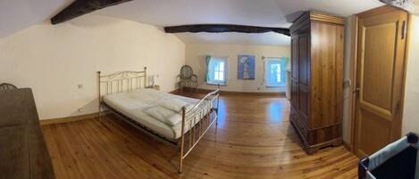 A bedroom with a wooden floor, a bed, a wardrobe, and a chair.