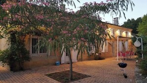 Une cour avec un chemin en briques, un petit arbre aux fleurs roses, un barbecue et un bâtiment doté d’un balcon.