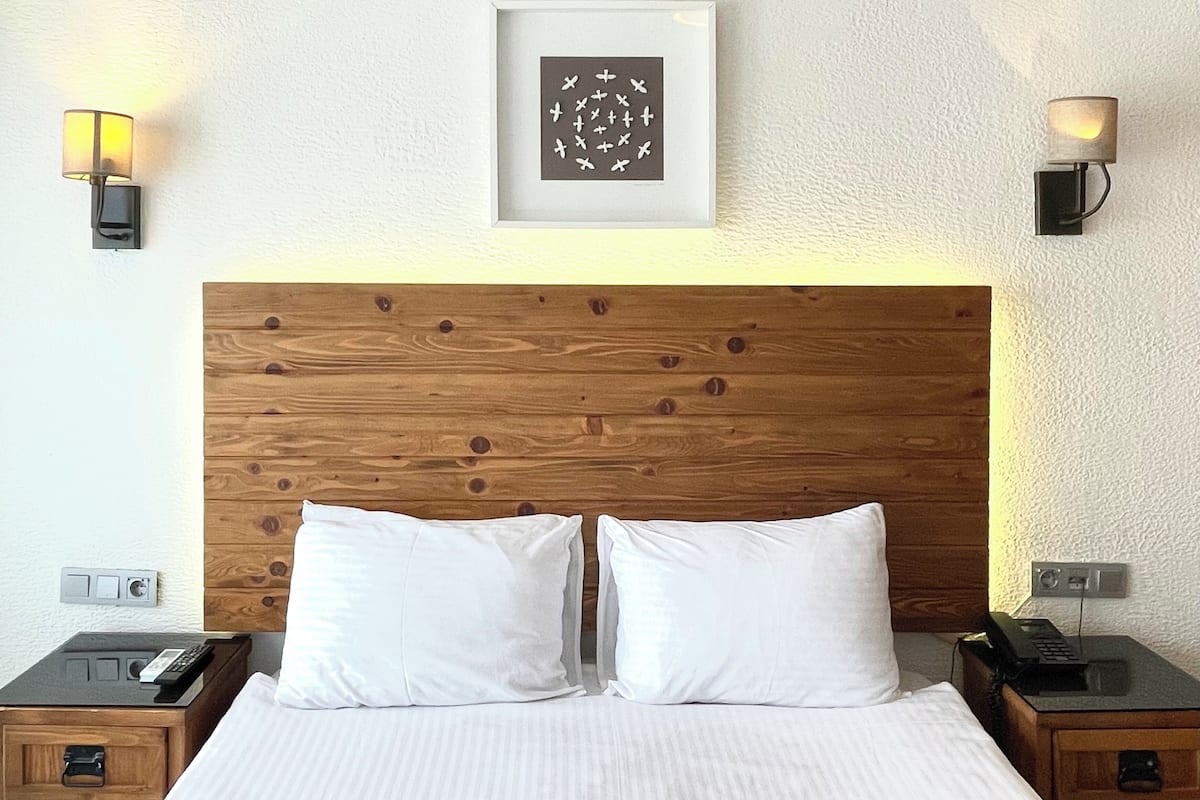 A hotel room with a wooden headboard, white bedding, two bedside tables with lamps, and a framed artwork on the wall.
