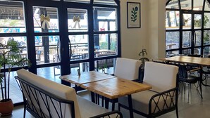 A café interior with high arched windows, wooden tables, and black metal chairs. - 8 Rooms Hotel (Gallipoli)