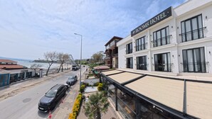 A hotel with a sign reading 'Rooms Hotel,' a paved street, parked cars, and a view of the sea. - 8 Rooms Hotel (Gallipoli)