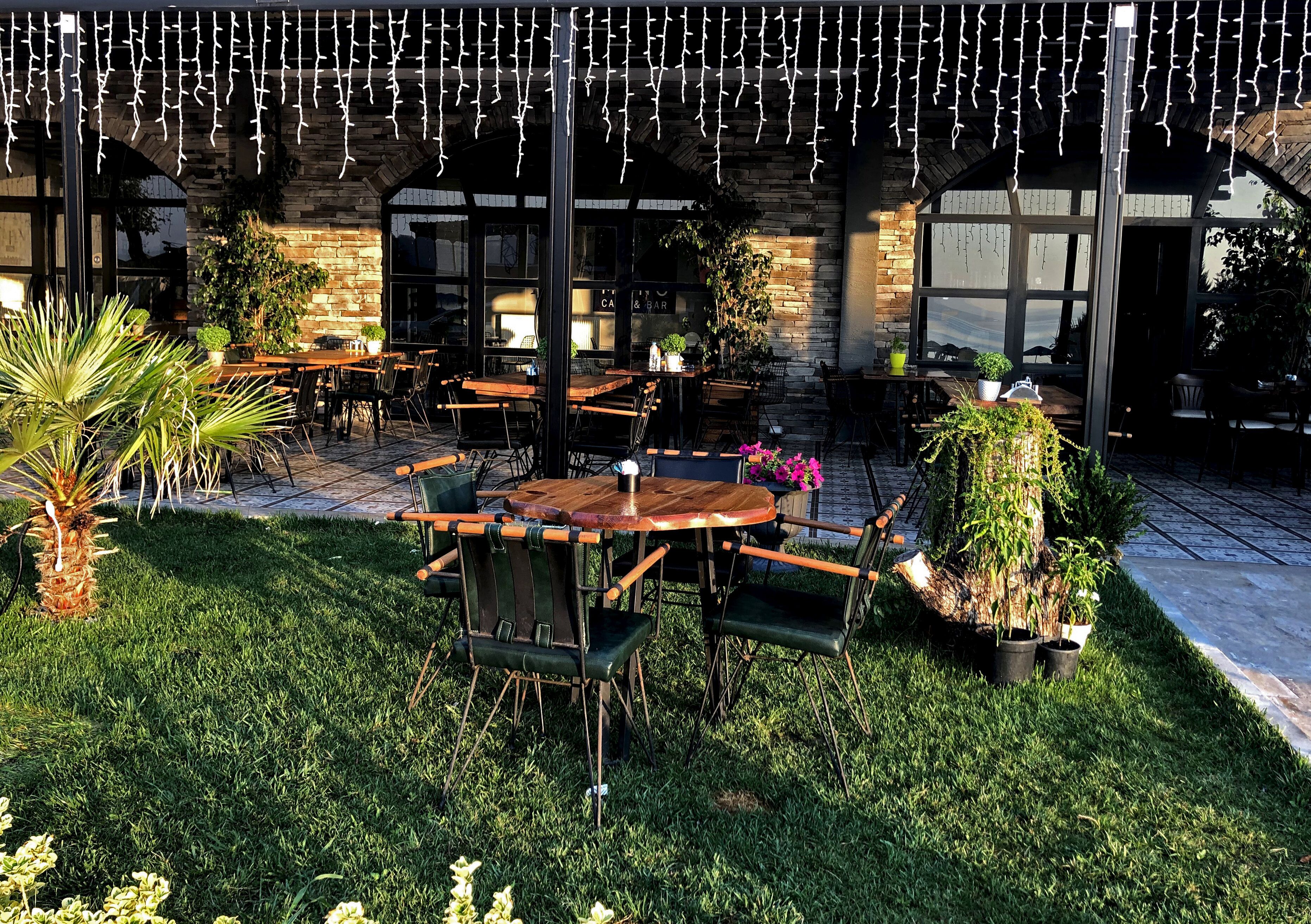 An outdoor seating area with tables and chairs, surrounded by greenery and potted plants.