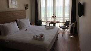 A hotel room with a large bed, a small table with chairs, a view of the sea through the window, and a television mounted on the wall. - 8 Rooms Hotel (Gallipoli)
