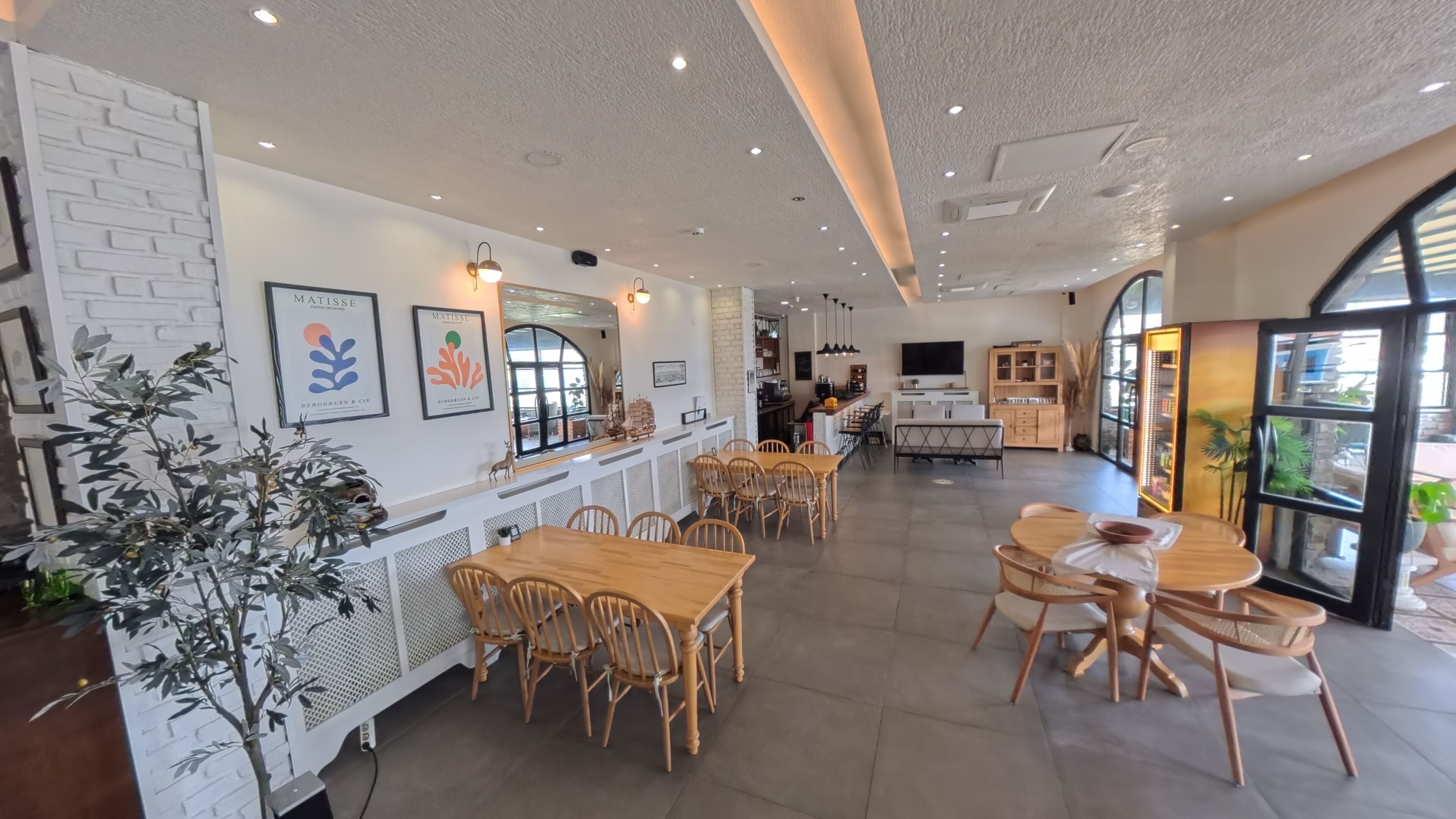 Un interior de restaurante moderno con mesas y sillas de madera, una barra con menú y obras de arte enmarcadas en las paredes.