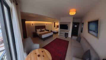 A modern hotel room with a bed, sofa, TV, and a red rug.