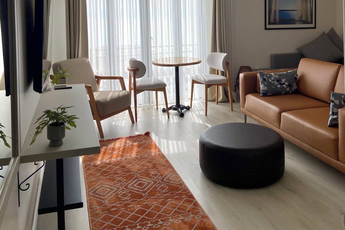 A modern living room with a round table, two chairs, a sofa, a TV, and a painting on the wall.