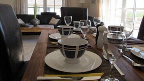 Un comedor con una mesa de madera dispuesta para una comida, un sofá negro y una ventana con cortinas.