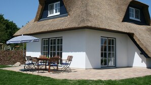 Una casa con techo de paja, ventanas grandes y un patio con muebles de exterior.