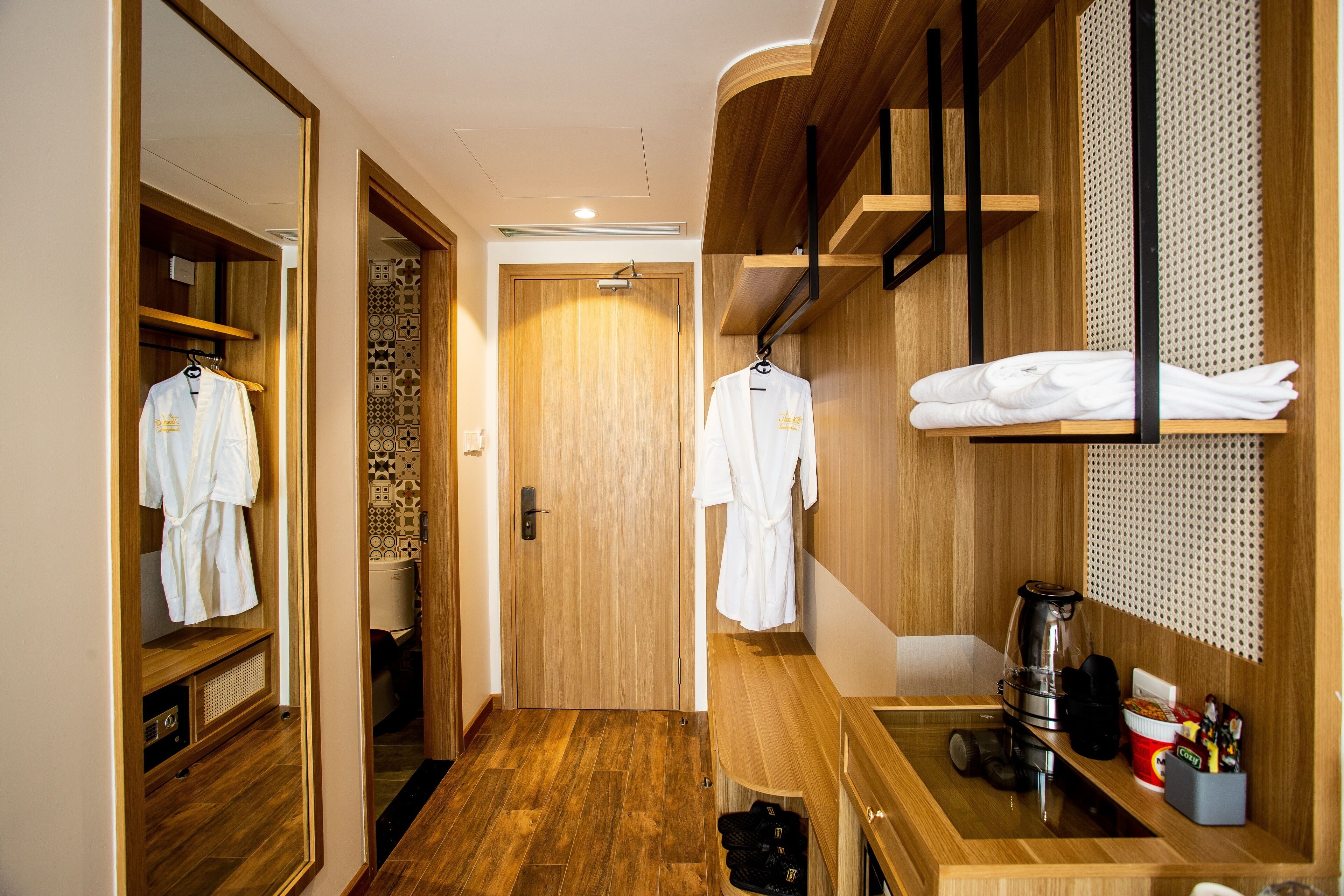 A hotel room with a wooden floor, a mirror, a wooden vanity with a sink, and a towel rack.