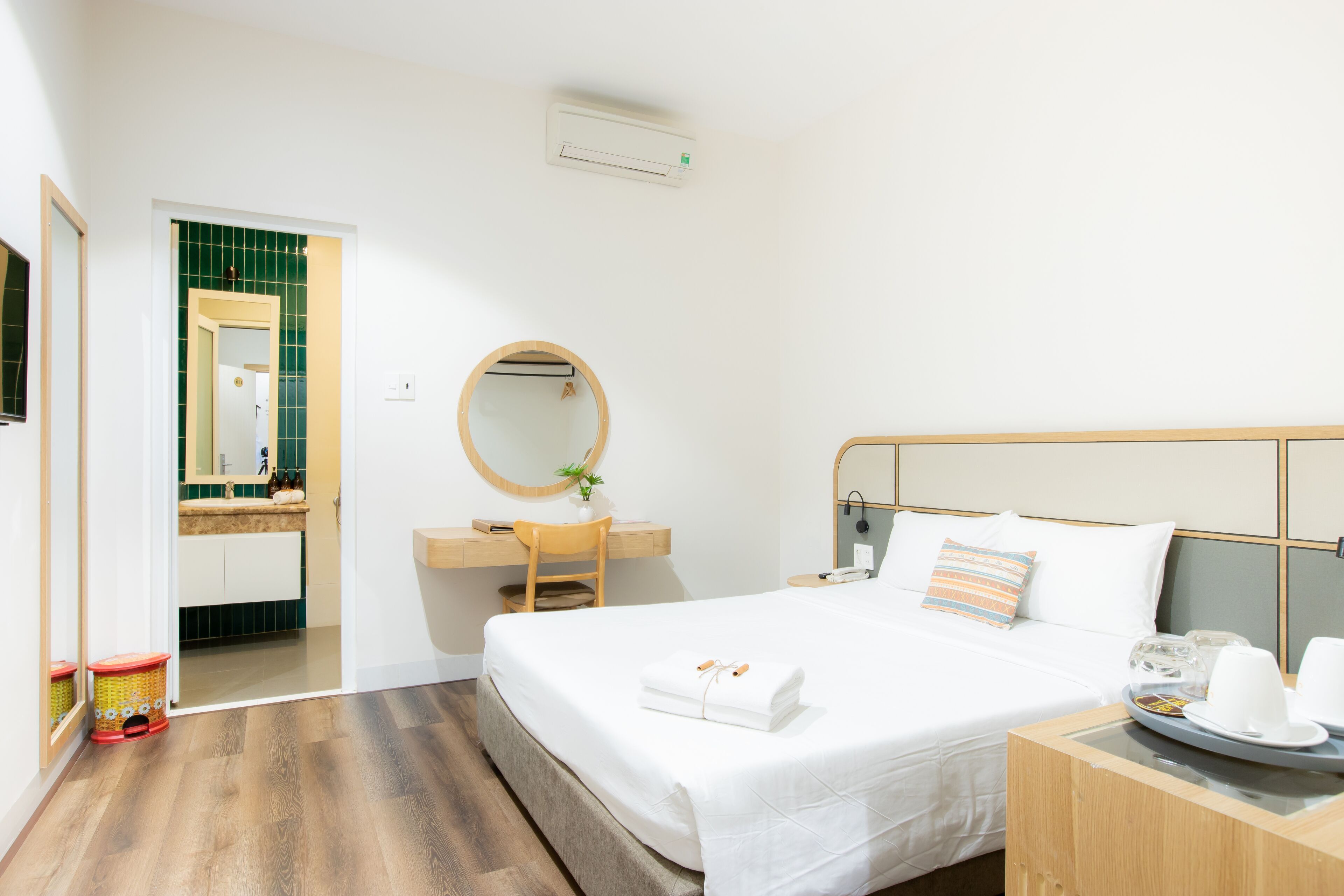 A hotel room with a bed, a desk, a chair, a round mirror, and a small table with cups and a tray.