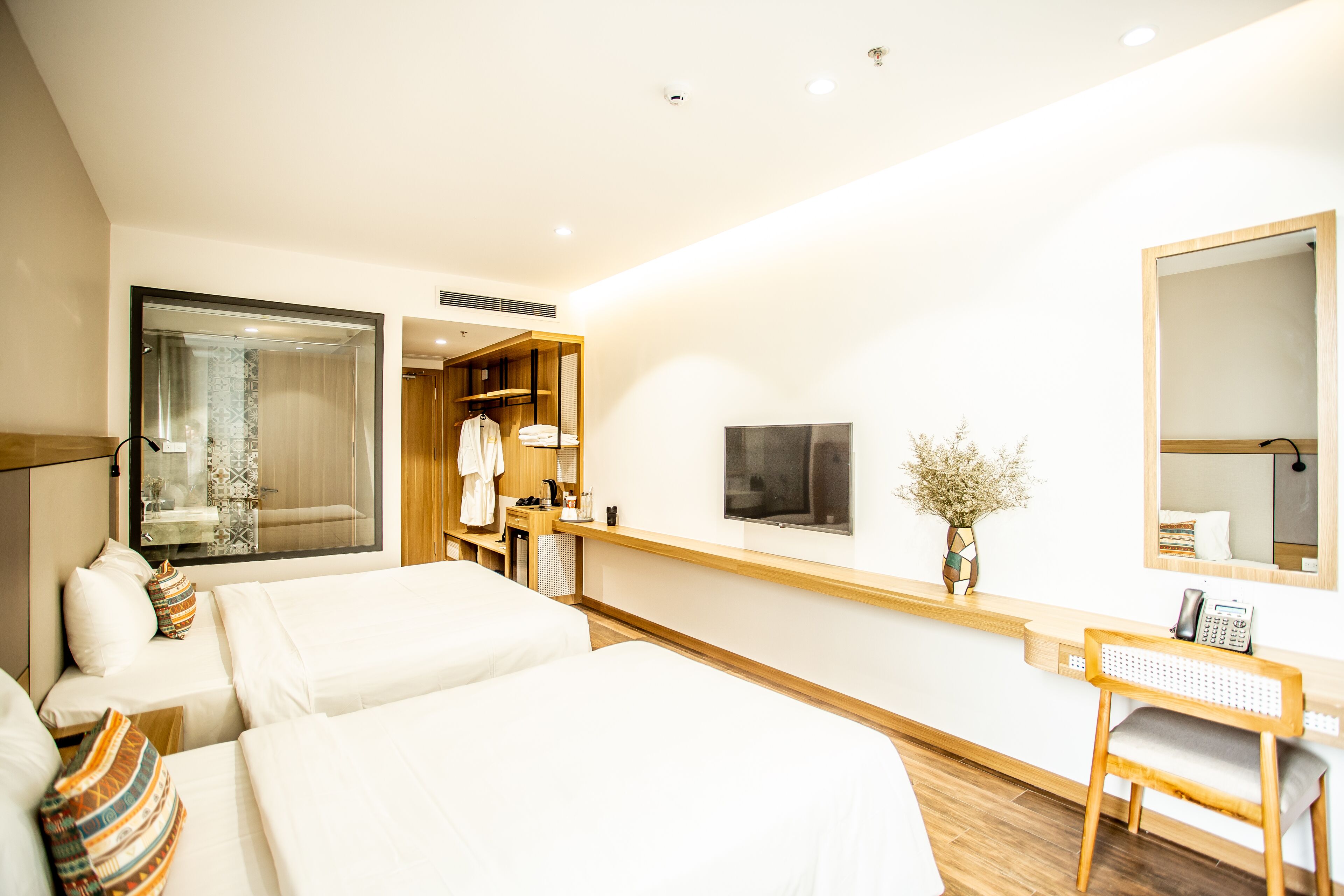 A hotel room with two beds, a desk, a mirror, and a TV.
