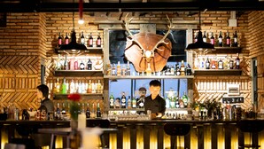 Un bar avec un grand crâne de cerf accroché au mur, des étagères remplies de bouteilles d’alcool et un barman derrière le comptoir.