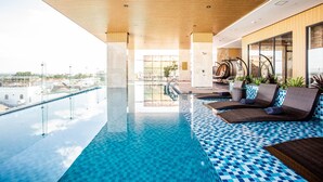 Une piscine à débordement moderne, dotée d’un plafond en bois et d’une terrasse carrelée de bleu, offrant une vue imprenable sur le paysage urbain.