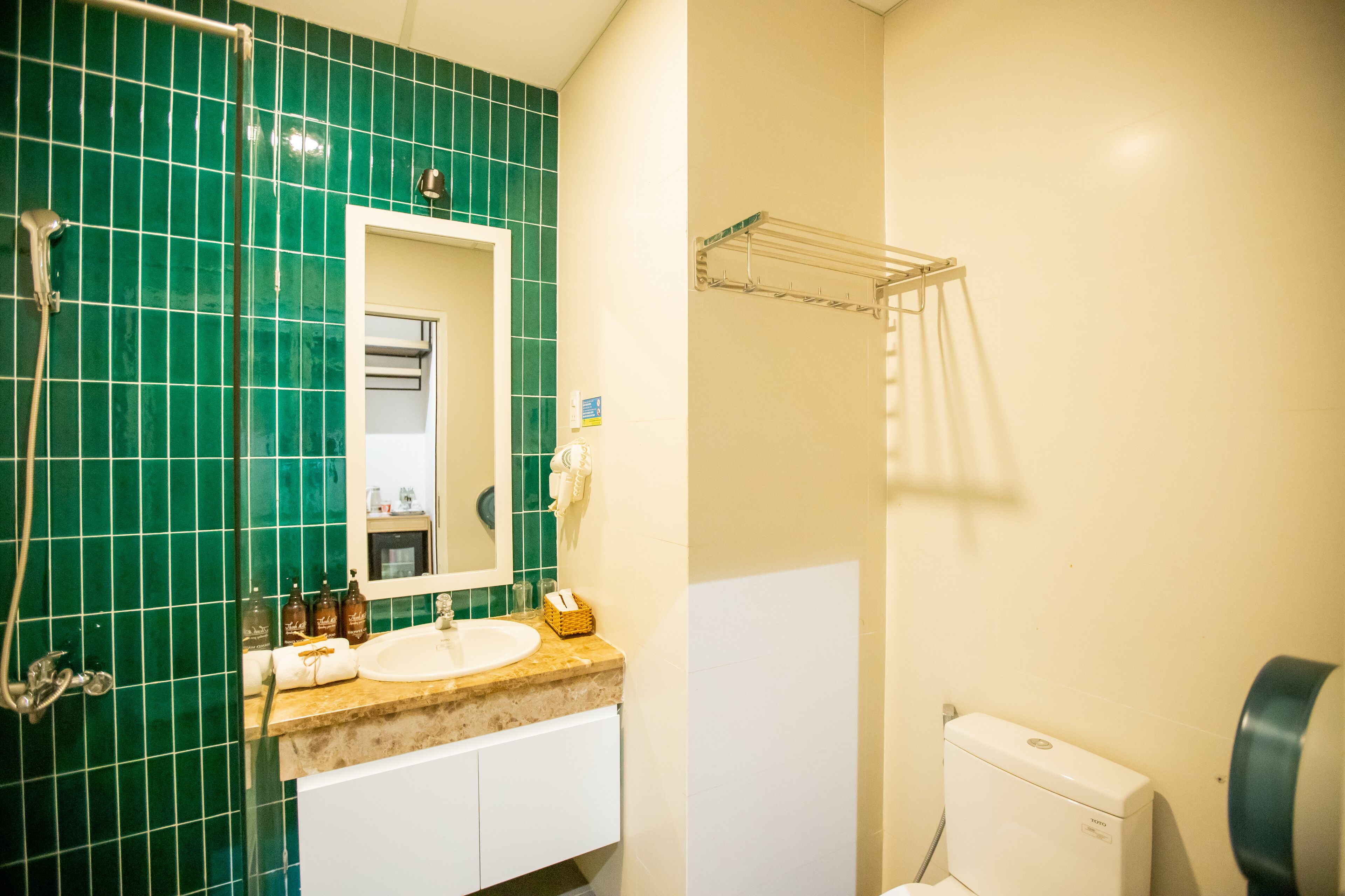 A bathroom with a green tiled wall, a sink, a mirror, a towel rack, and a toilet.