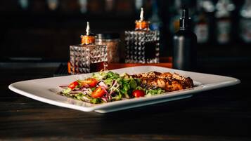A rectangular white plate with a salad and grilled chicken on a dark wooden table.