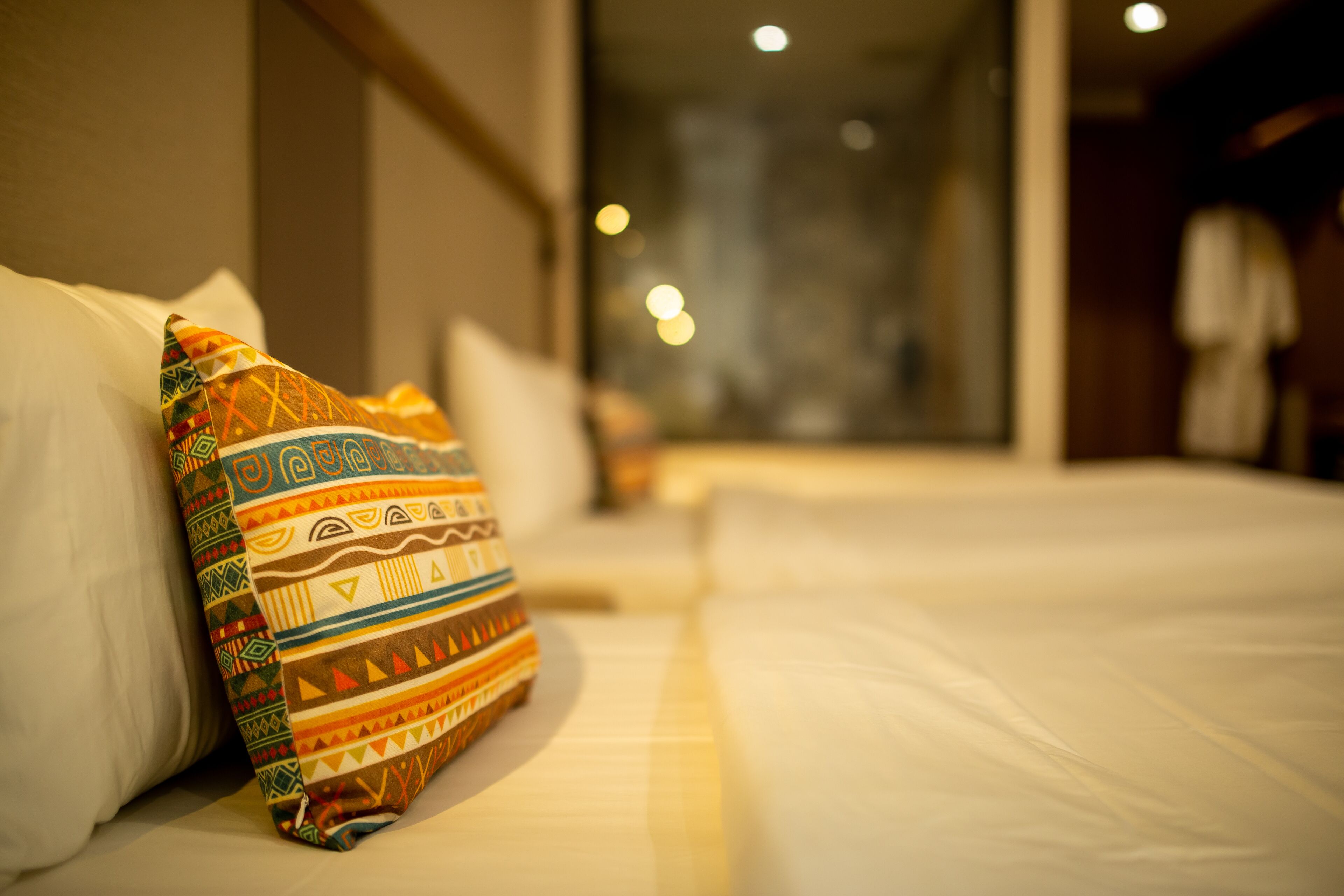 Un cuarto de hotel con una cama bien hecha, una almohada colorida y una ventana con vista a la ciudad.